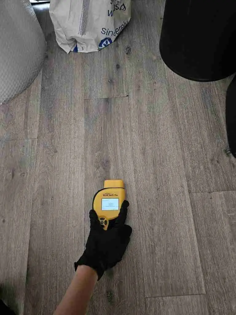 Rapid Response technician checking a wood floor with a moisture meter near a plumbing leak