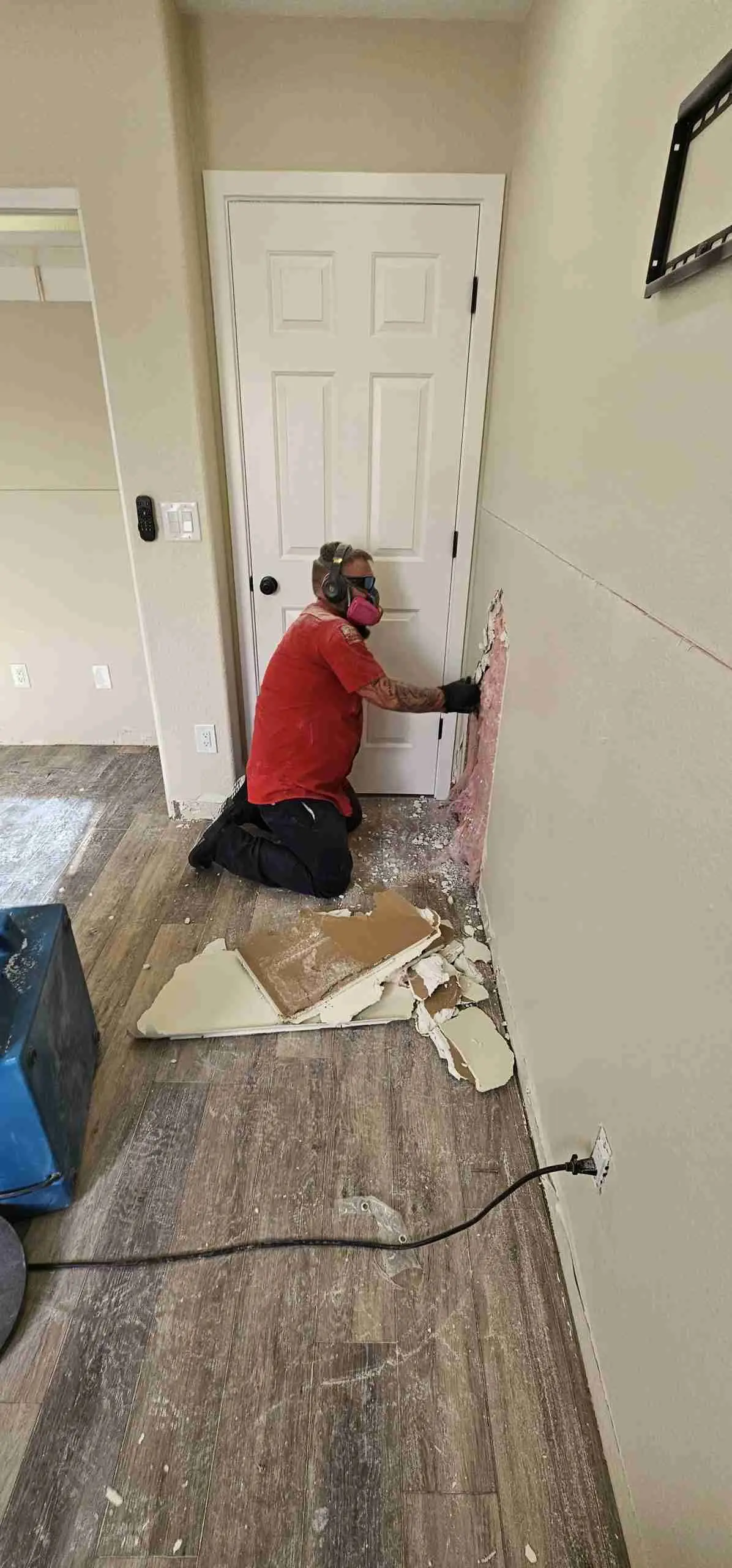 Technician cutting out water-damaged drywall at floor level