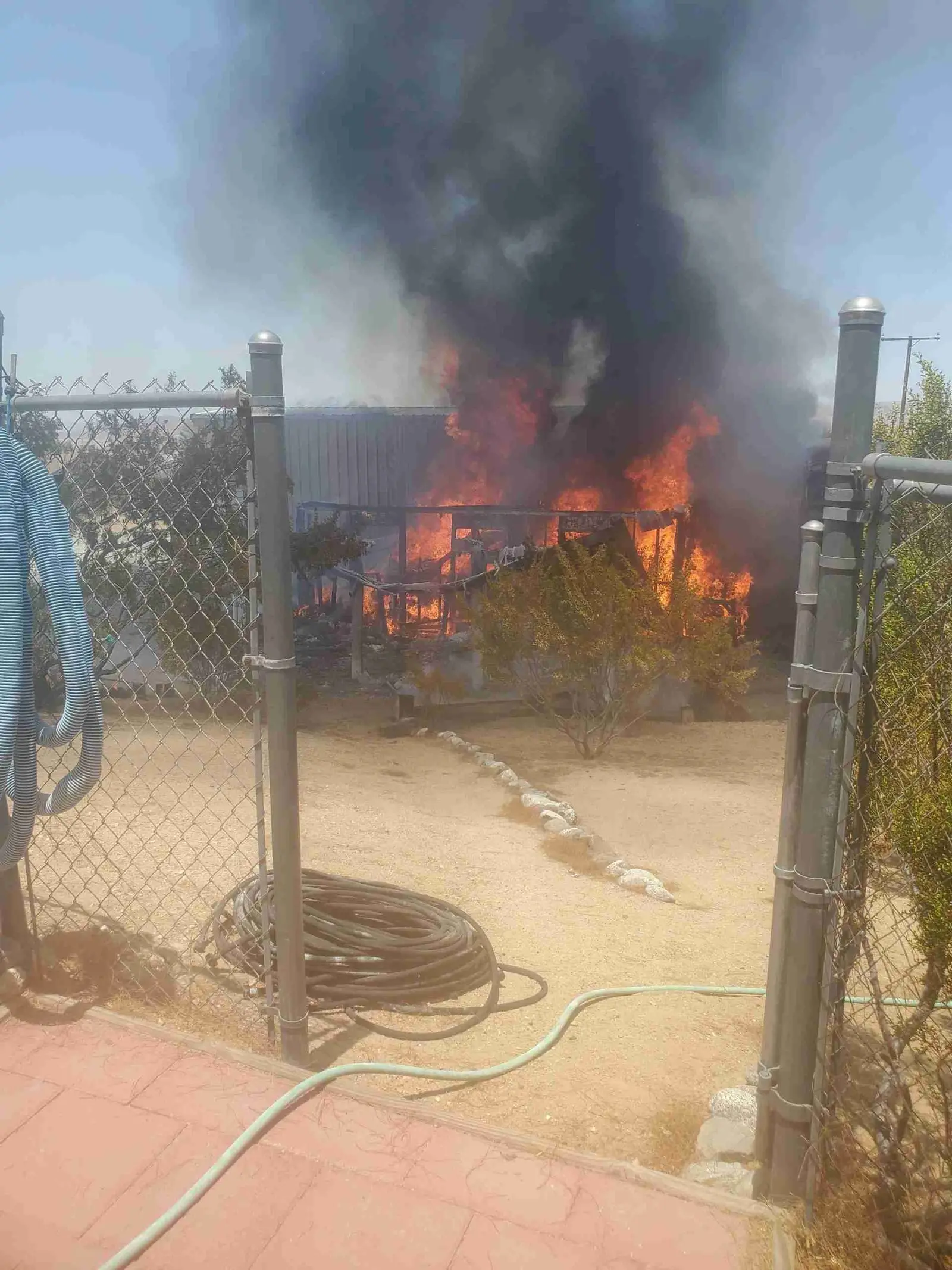 Structure fire with heavy black smoke behind a chain-link fence