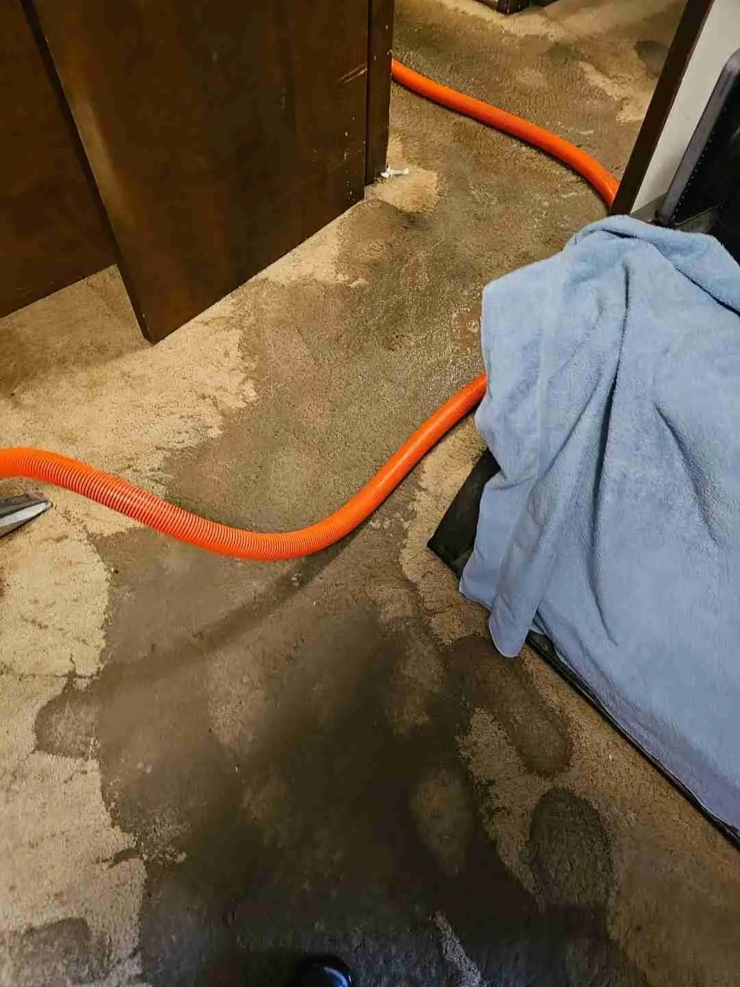 Water-stained floor with an extraction hose during cleanup after a backup on a Rapid Response job